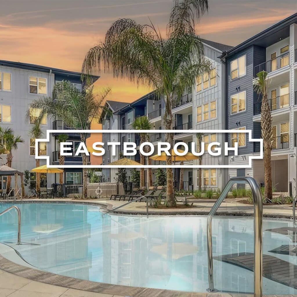 Pool area at Eastborough apartment complex, featuring palm trees and multi-story buildings under a sunset sky.