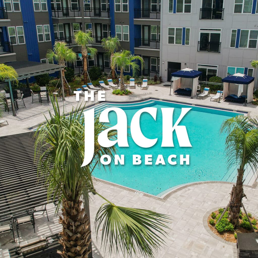 Pool area of The Jack on Beach apartment complex, with palm trees and lounge chairs around the water.